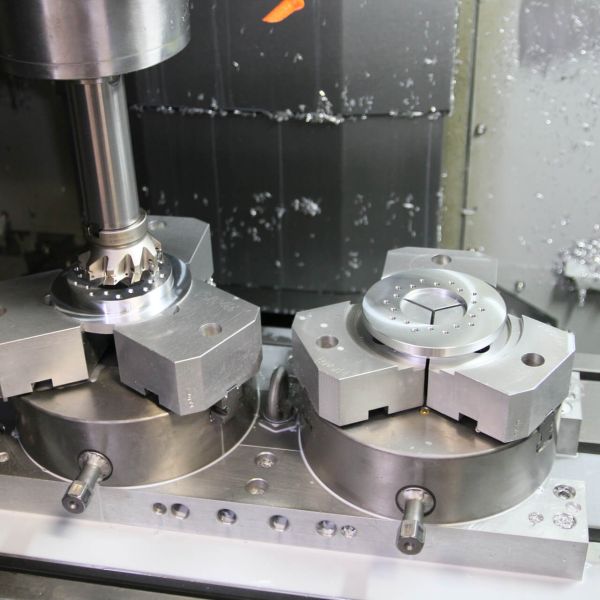 Luftaufnahme eines großen Industrie- oder Bürogebäudes mit weißem Dach, umgeben von geparkten Autos, Grünflächen und anderen Gebäuden in der Nähe in einer ländlichen Gegend.