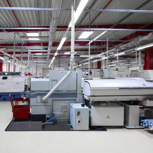 Luftaufnahme eines großen Industrie- oder Bürogebäudes mit weißem Dach, umgeben von geparkten Autos, Grünflächen und anderen Gebäuden in der Nähe in einer ländlichen Gegend.