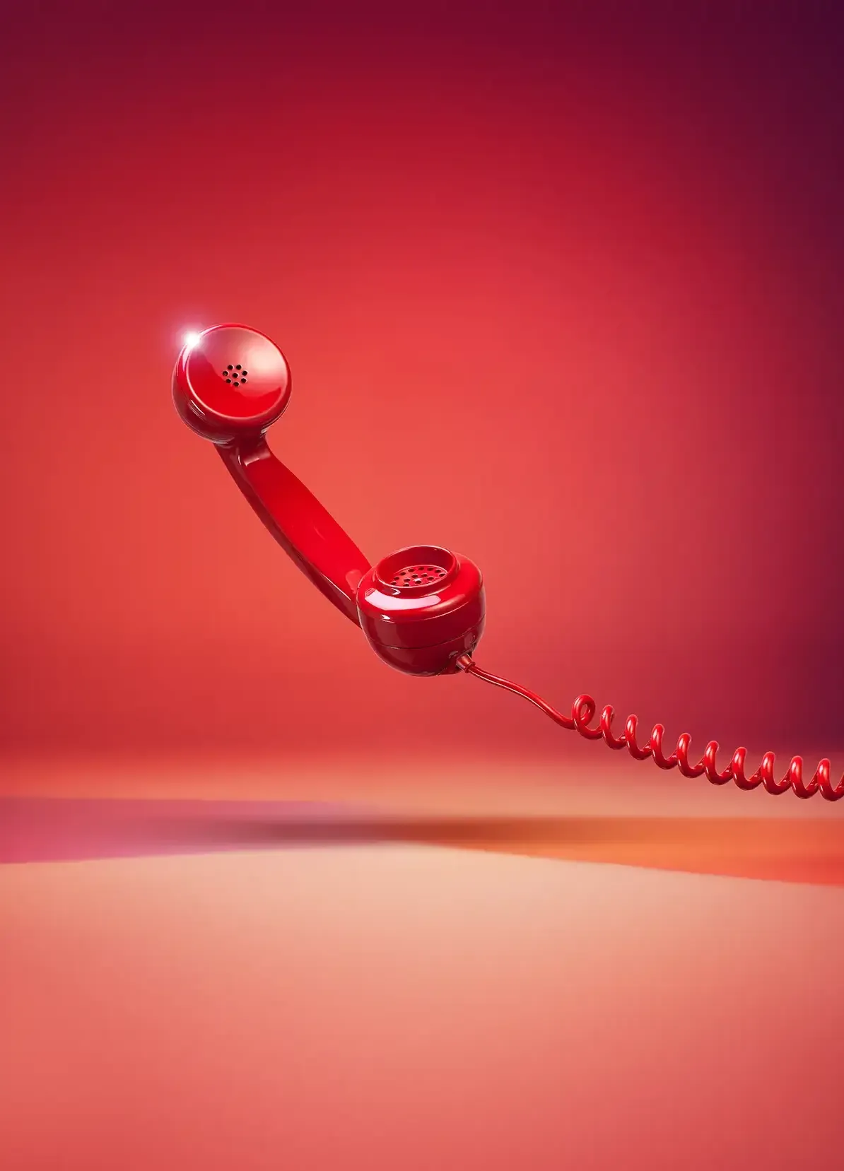 Ein glänzender roter Retro-Telefonhörer mit einer gewundenen Schnur hängt vor einem roten und rosafarbenen Hintergrund und wirft einen weichen Schatten darunter.