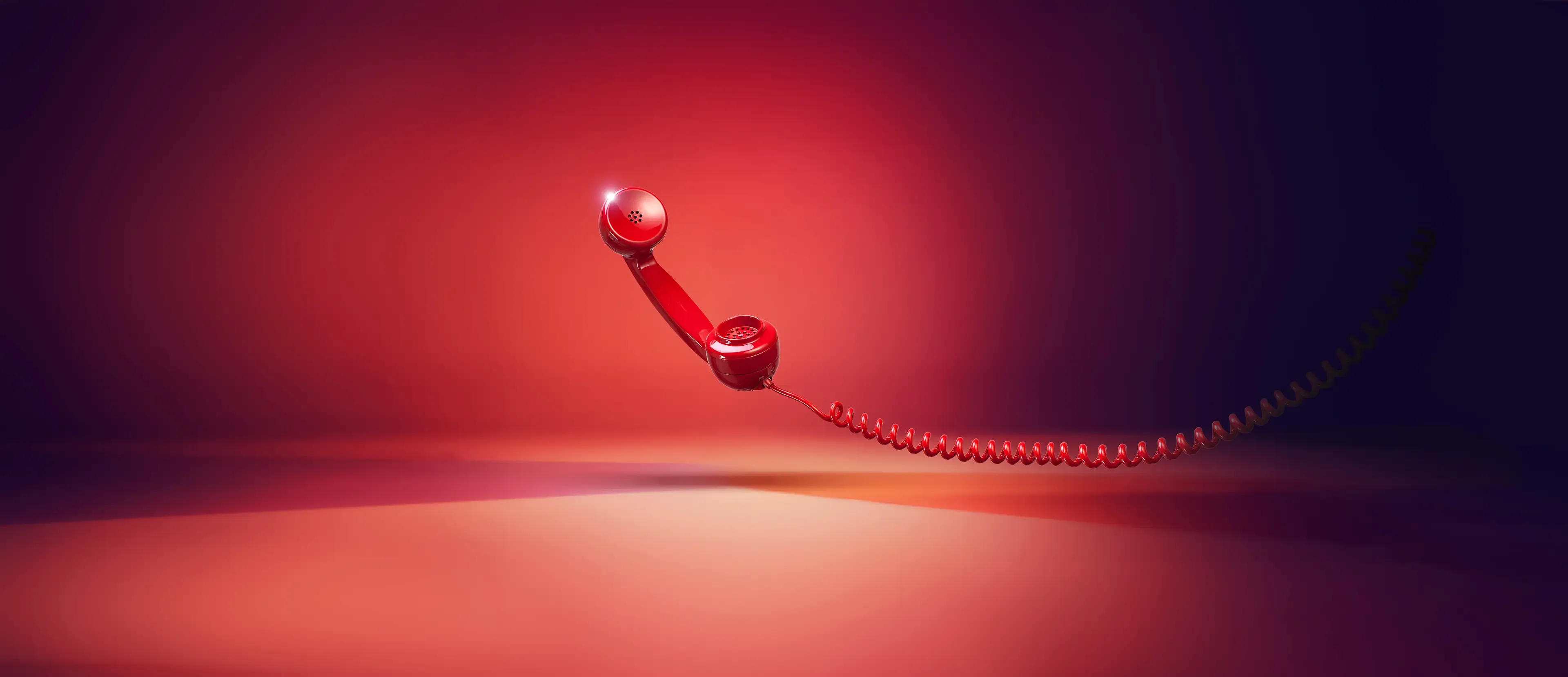 Ein roter Telefonhörer mit einer aufgewickelten Schnur schwebt in der Luft vor einem roten und violetten Hintergrund, der einen weichen Schatten auf die darunter liegende Fläche wirft.
