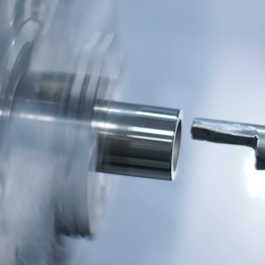 Nah­auf­nahme einer CNC-Dreh­maschine, die einen rotierenden Metall­zylinder schneidet und dabei glatte und glänzende Ober­flächen­konturen erzeugt. Der Hinter­grund ist unscharf und unter­streicht den Präzisions­metall­bearbeitungs­prozess.