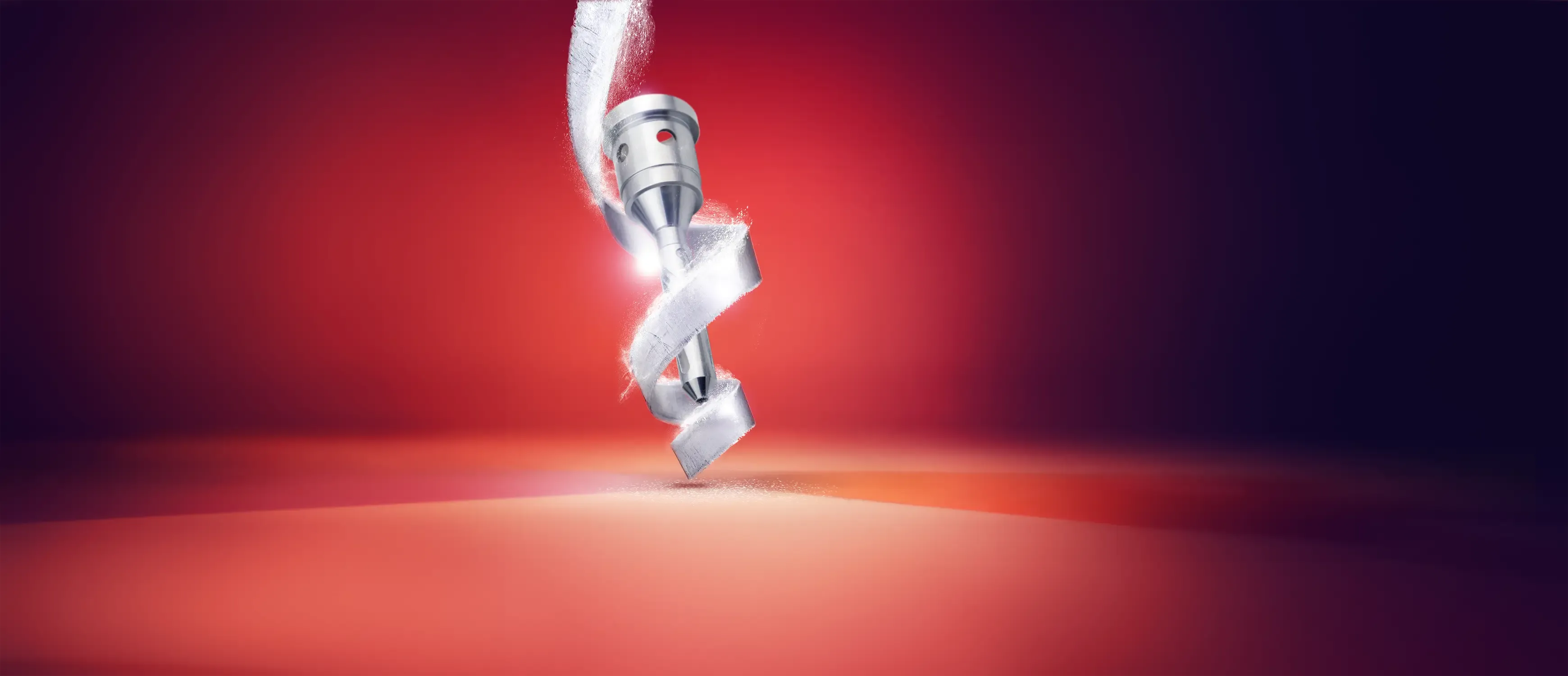 Eine Nahaufnahme eines glänzenden Metallbohrers, der spiralförmig in eine glatte rote Oberfläche eindringt und einen kleinen Staubhaufen erzeugt, wobei ein glühendes Licht den Bohrer vor einem roten Hintergrund hervorhebt.
